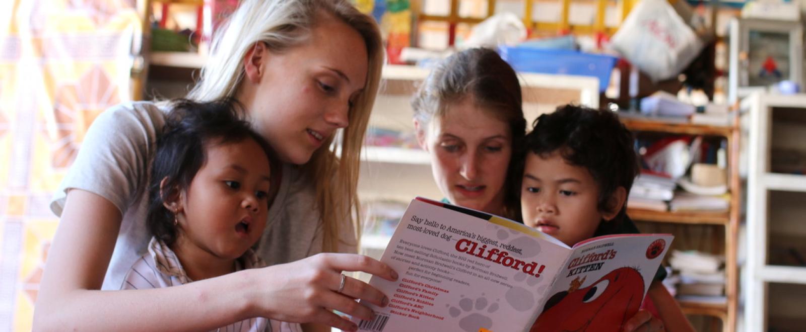 Female volunteers on the Projects Abroad Childcare Programme read a book to two local Cambodian children.