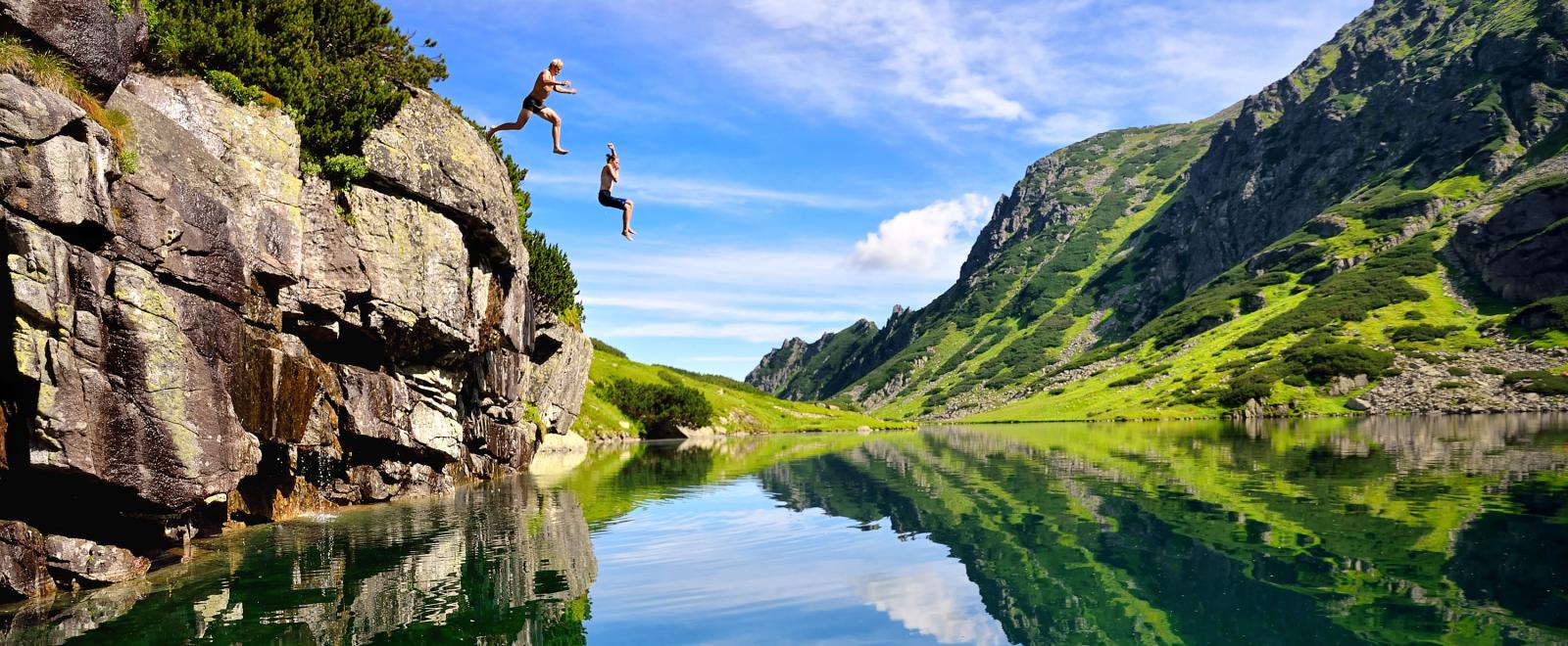 Two travellers enjoy their adventure by jumping off a cliff into water