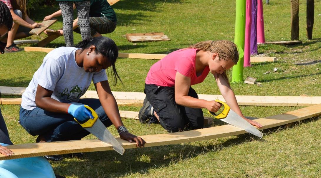 Two women work together to saw wood to build playground equipment during their volunteer building work abroad.