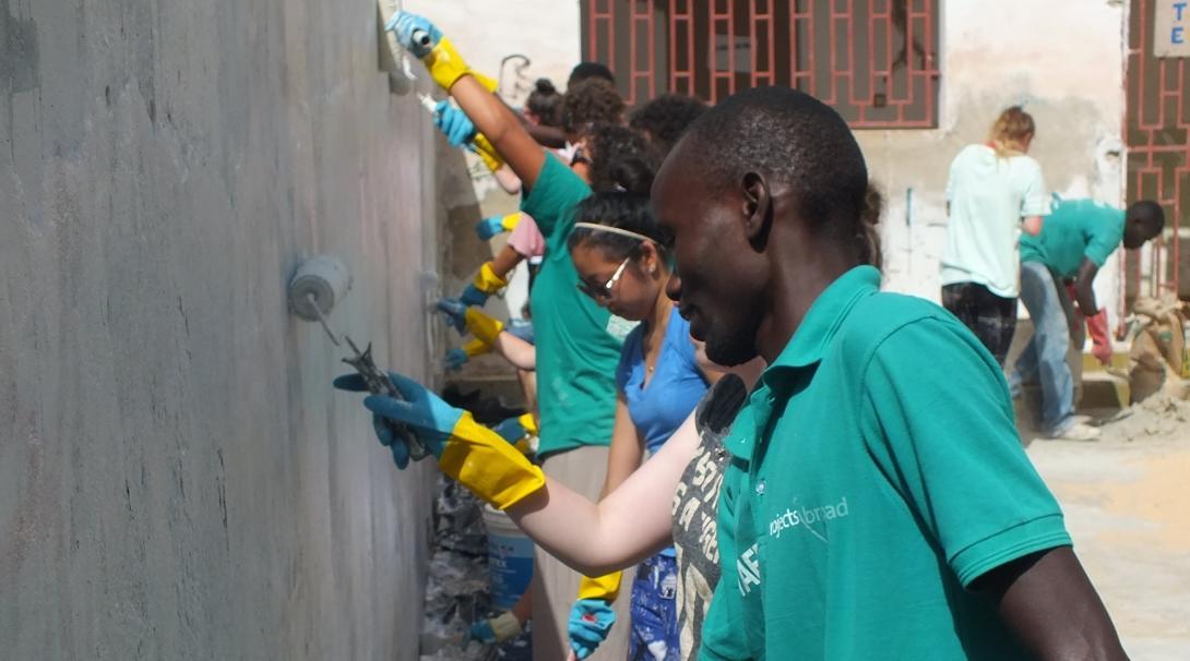 A staff member supports volunteers as they paint a newly constructed wall on one of our volunteer building projects