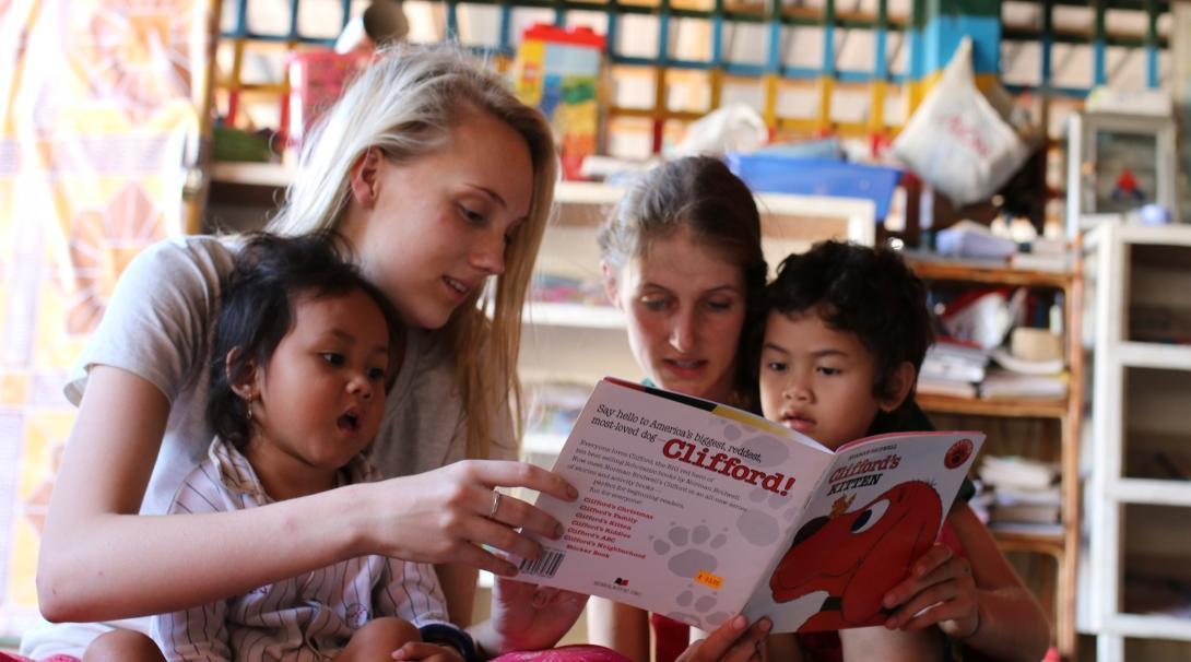 Cambodian children read aloud with two Childcare volunteers working abroad at a kindergarten,