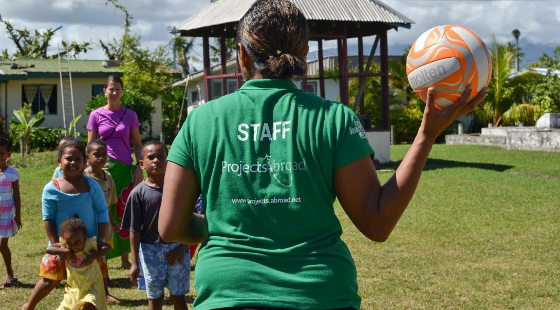 A staff member guides volunteers through a sports lesson while they are working with children abroad.