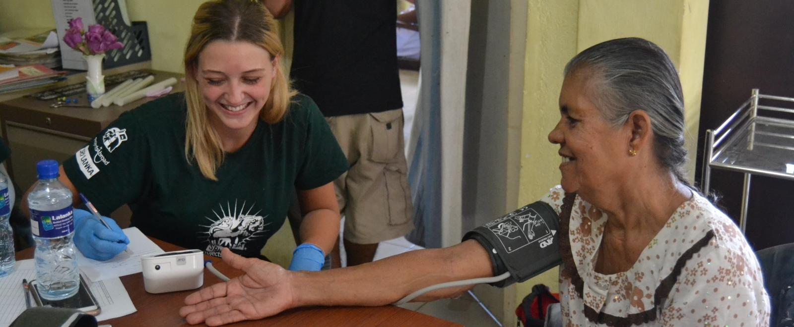 During outreach work in Sri Lanka, a public health intern takes a woman’s blood pressure reading.