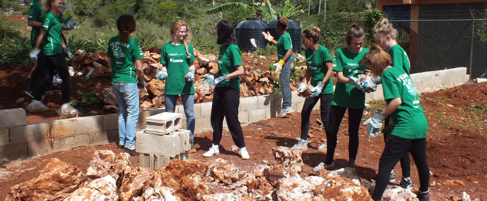 A group of people clear ground for a new playground at a disadvantaged school during their short-term volunteer abroad trip to Jamaica. 