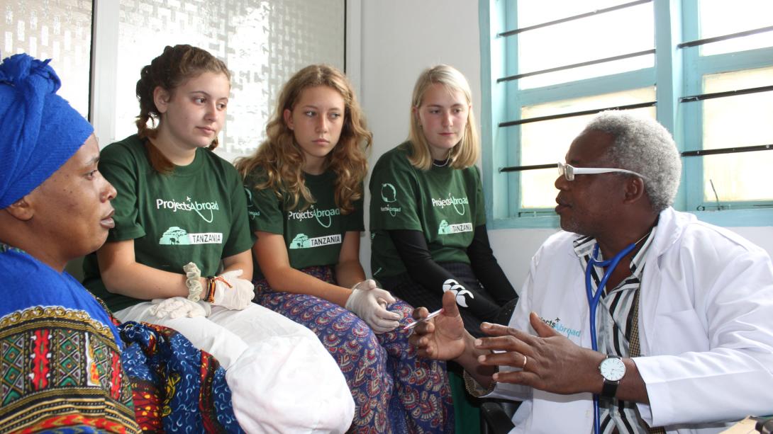 Medical interns in Tanzania listen to a doctor during a consultation with a woman