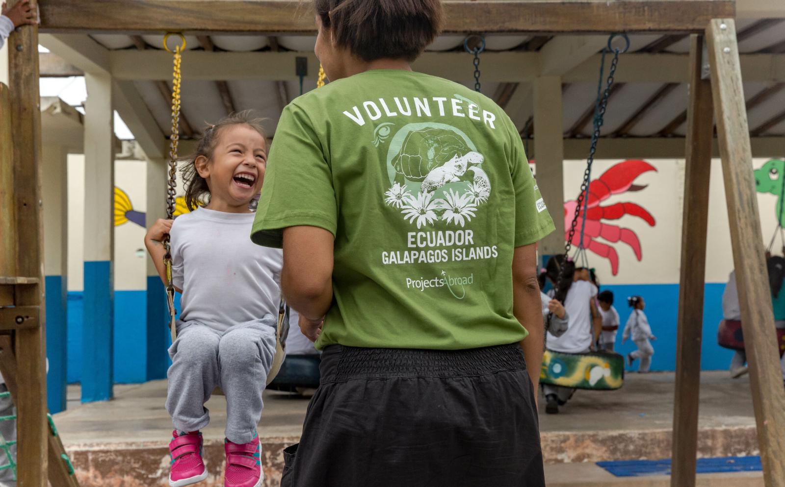 During volunteer work abroad with children in Ecuador a young child swings on the playground while a volunteer supervises