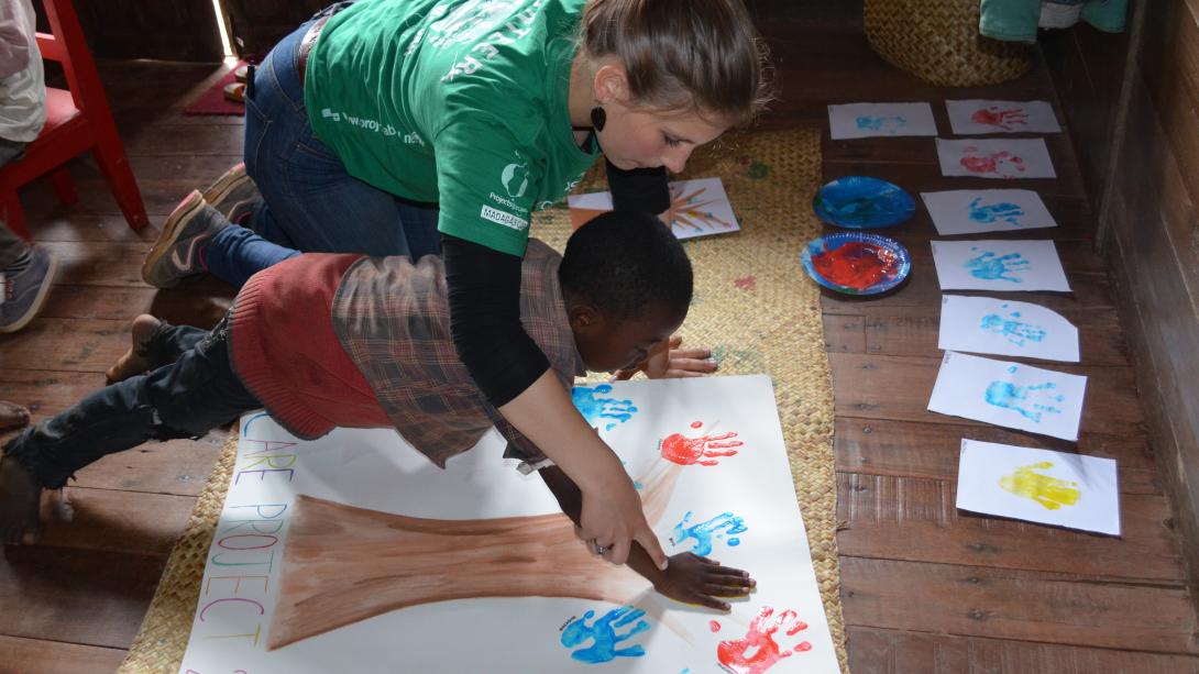 On a mission trip to Africa for high school students, a volunteer helps a child on an art project.