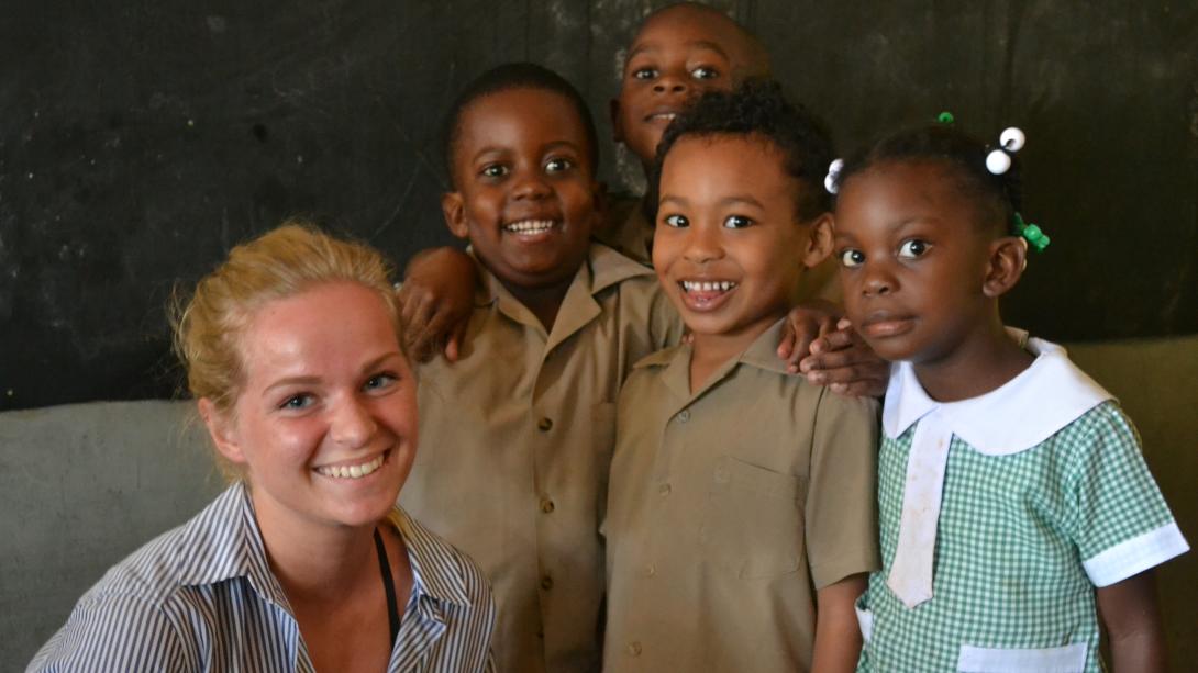 A short term volunteer teaching abroad takes a photo with her students in Jamaica