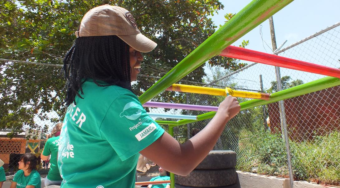 Youth Development volunteer paints a playground jungle gym in Jamaica.