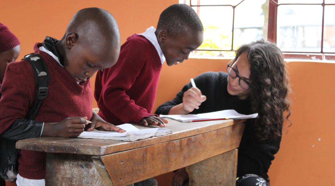 A volunteer teaching abroad helps children with their classwork in Tanzania. 