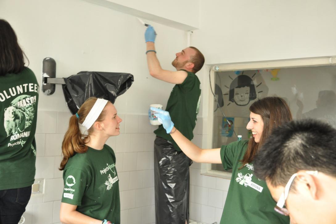 Smiling volunteer workers in Romania help to paint a room